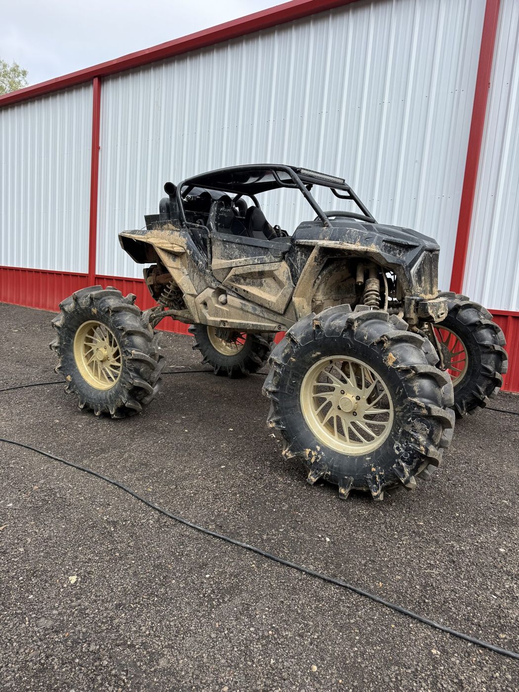 Polaris RZR caked in dried mud, parked outside the shop before cleaning